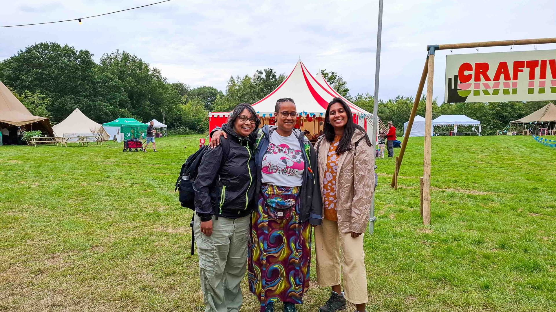 Three women stand together at the festival and smile.