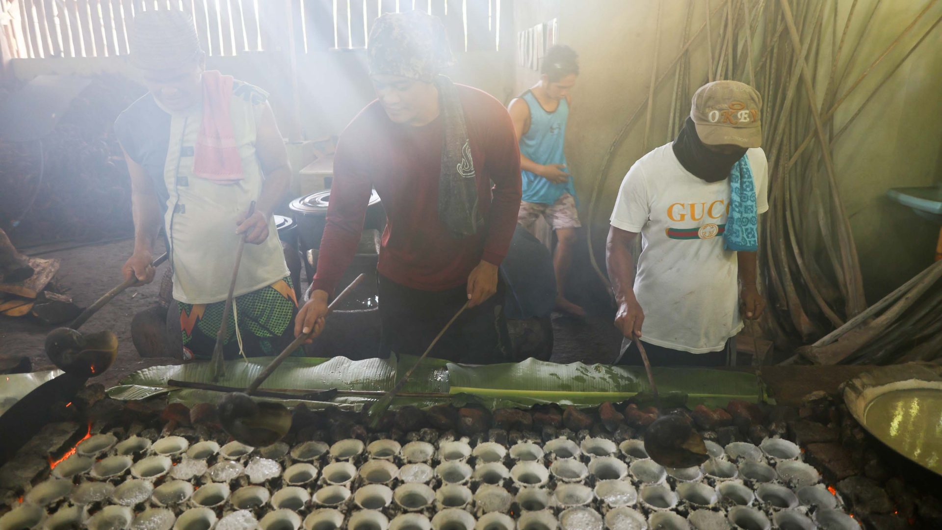 Men work in a row behind a table covered in salt balls. They are shrouded in smoke.