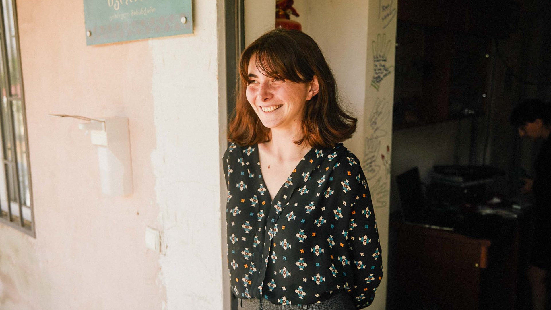 A woman stands in the door of her house and smiles.