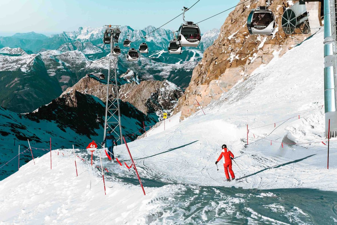 Snowy mountains in the background with cable cars above and skiers on the slopes.