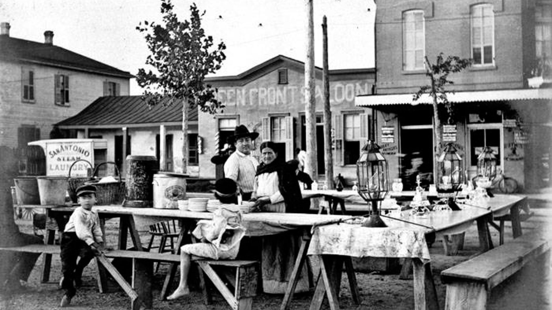 Two people stand amongst various tables at a chilli stand in a plaza.