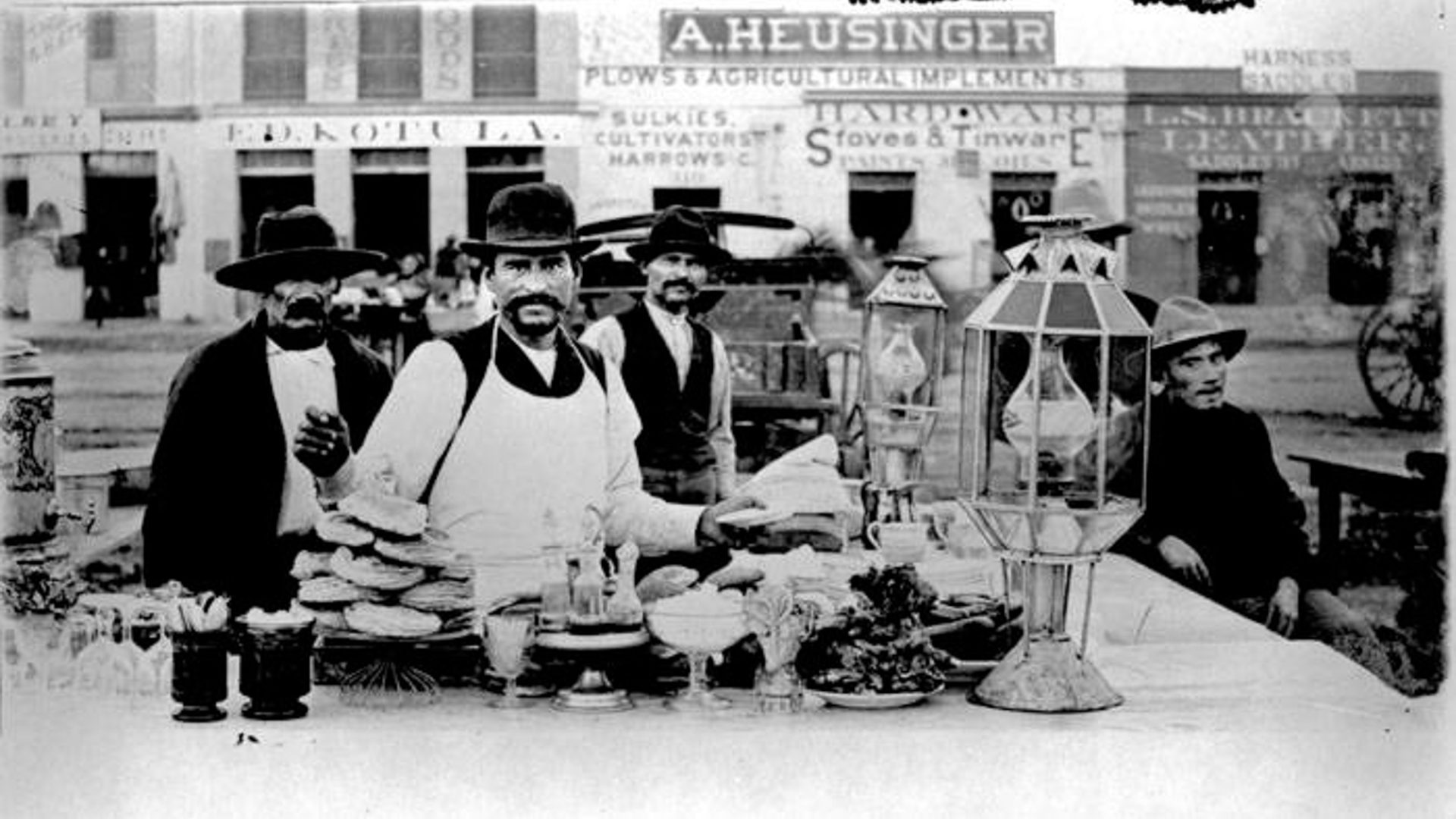 A black and white photo of three men working in a chilli food stand.