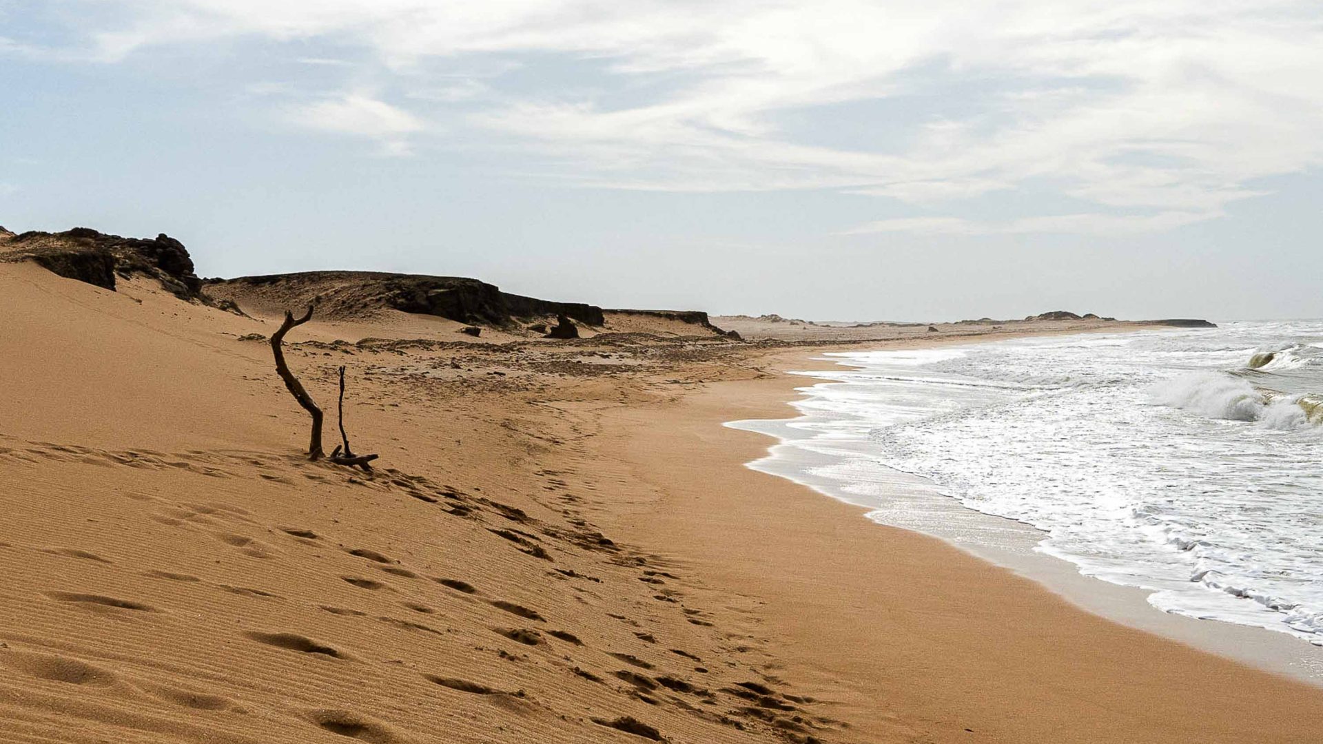 Sand dunes come down to the waters edge which has footprints along the length of it.