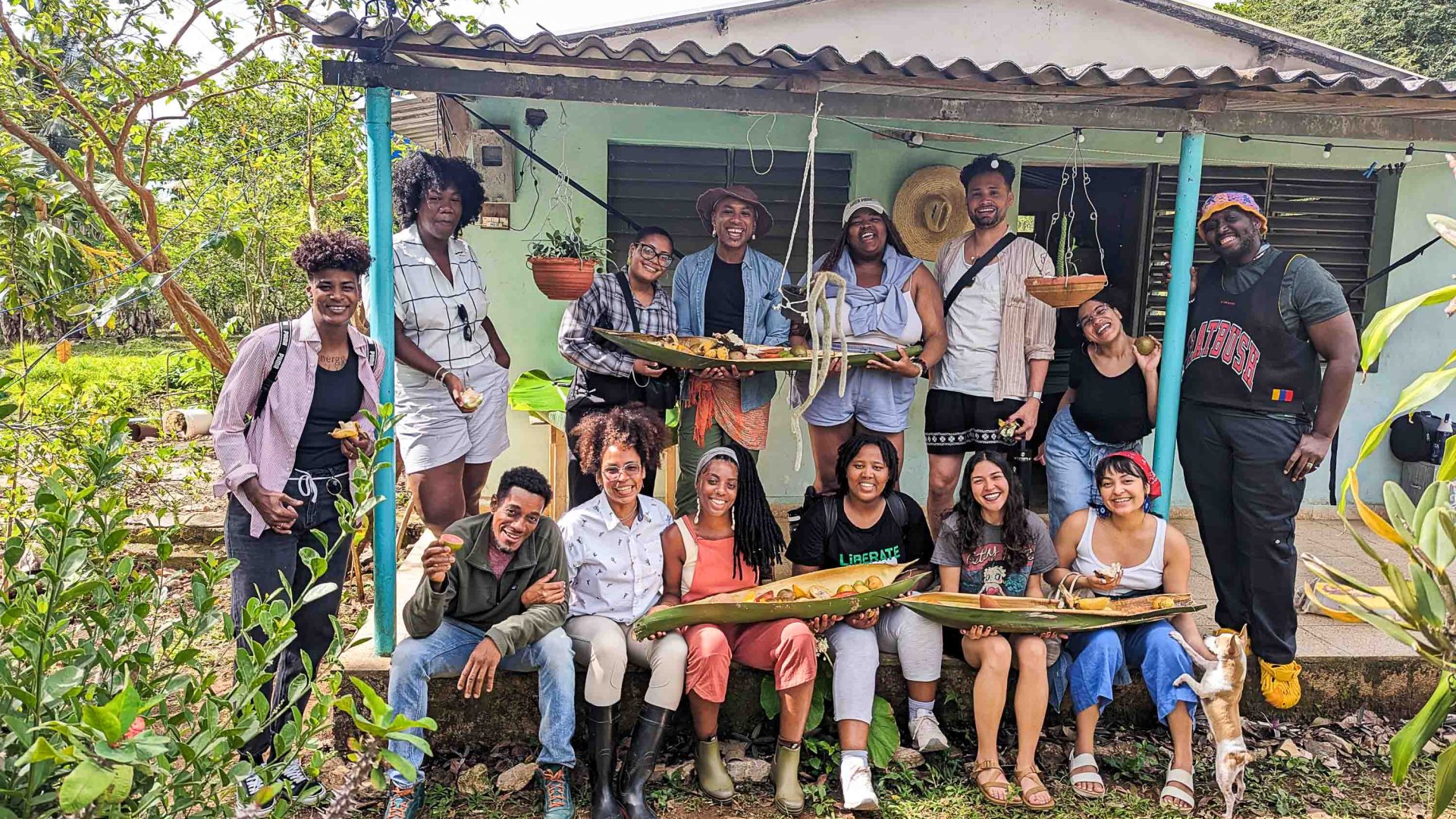 A group of people holding vegetables stand in front of a house.