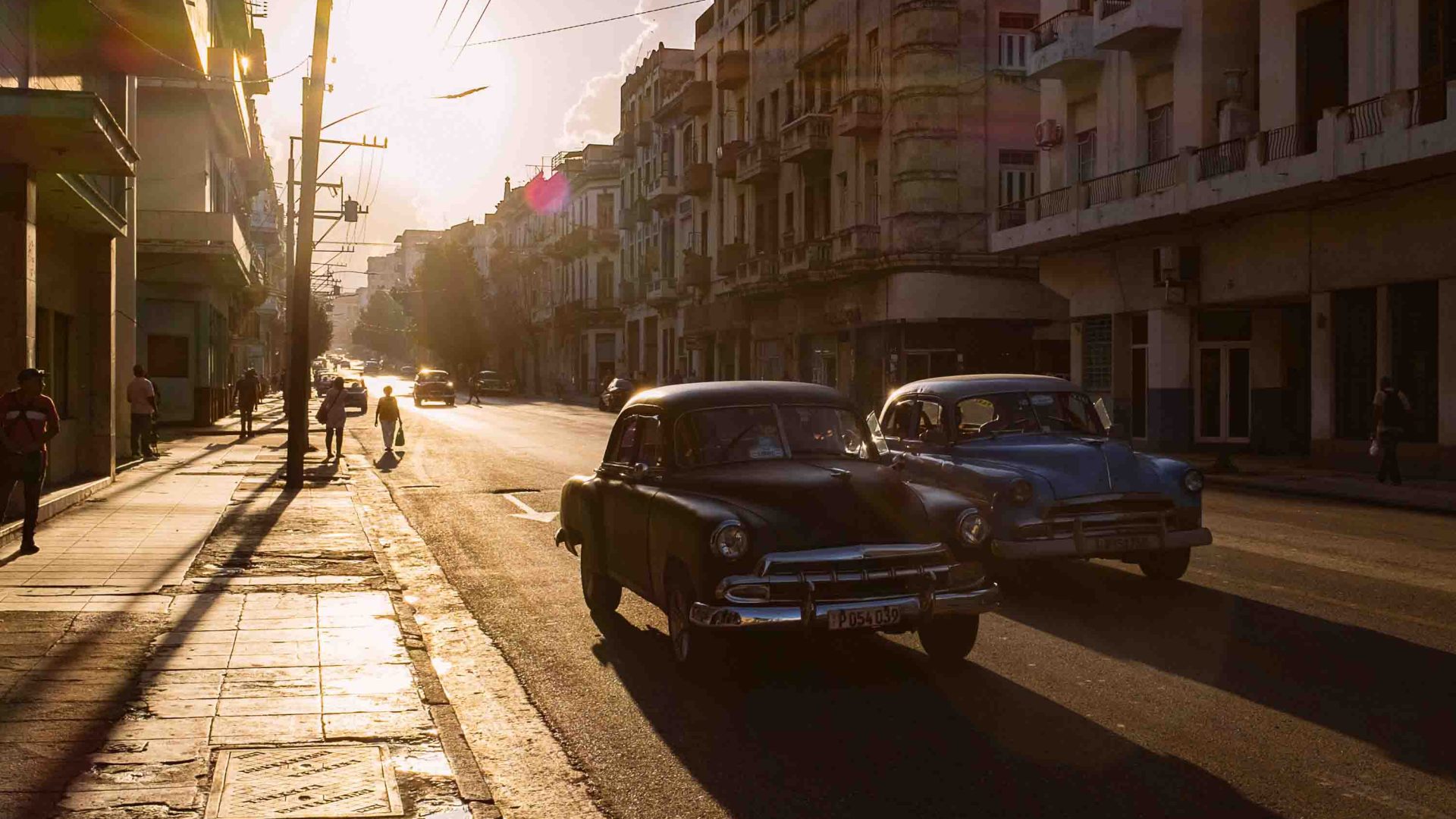 Soft light falling on a Havana street. Two cars drive down the street.