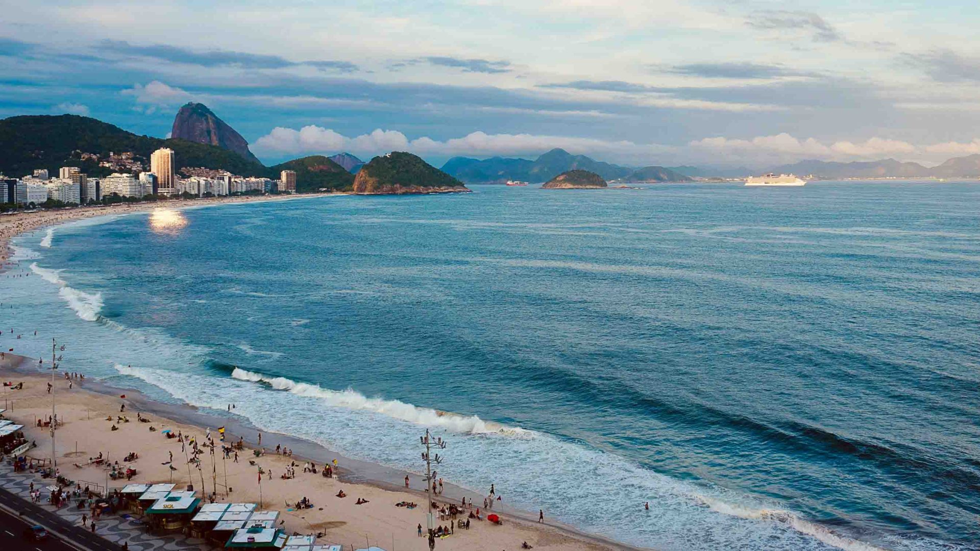 People on a beach with mountains and apartment buildings in the distance.