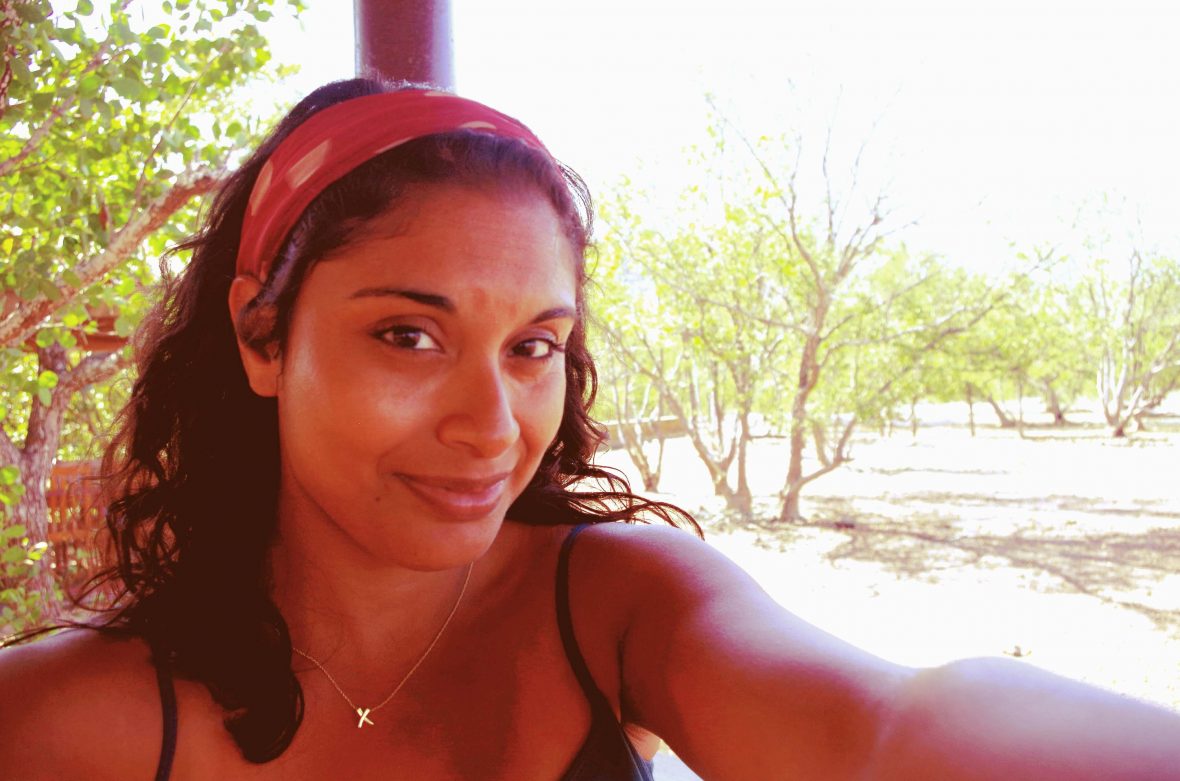 A womans with dark hair and a red hair band takes a selfie.