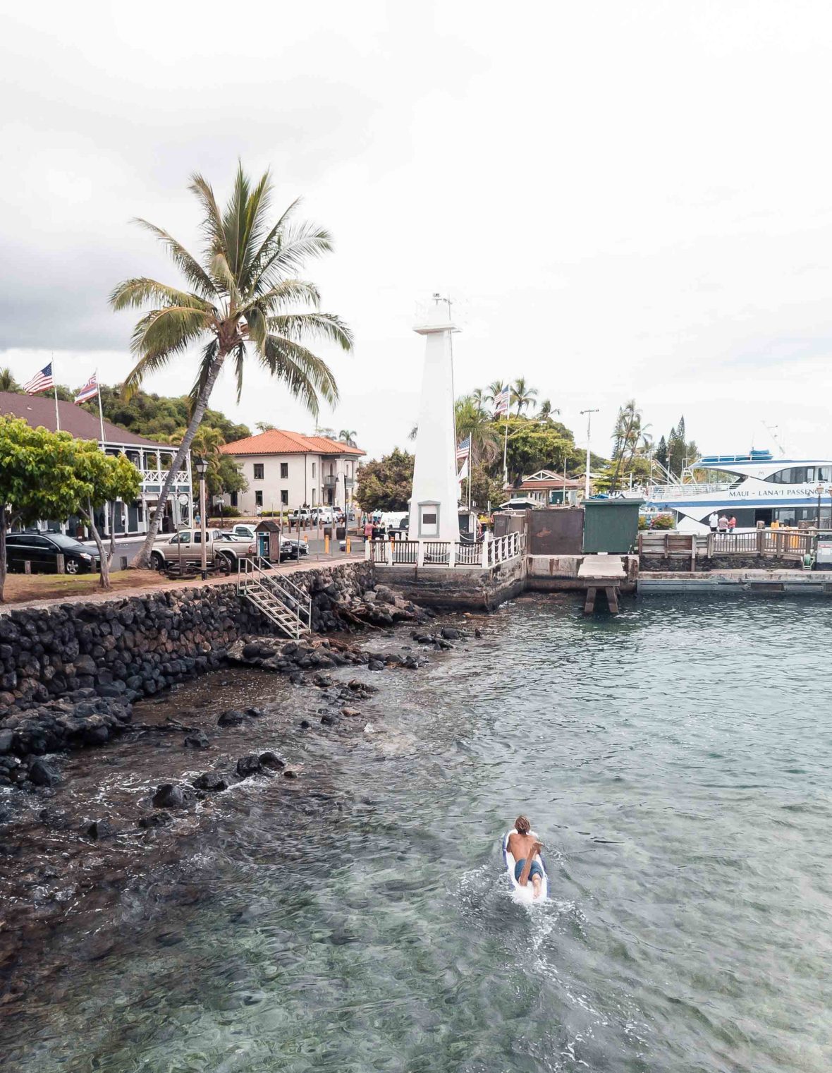 A surfer rides through the water towards a picturesque town.