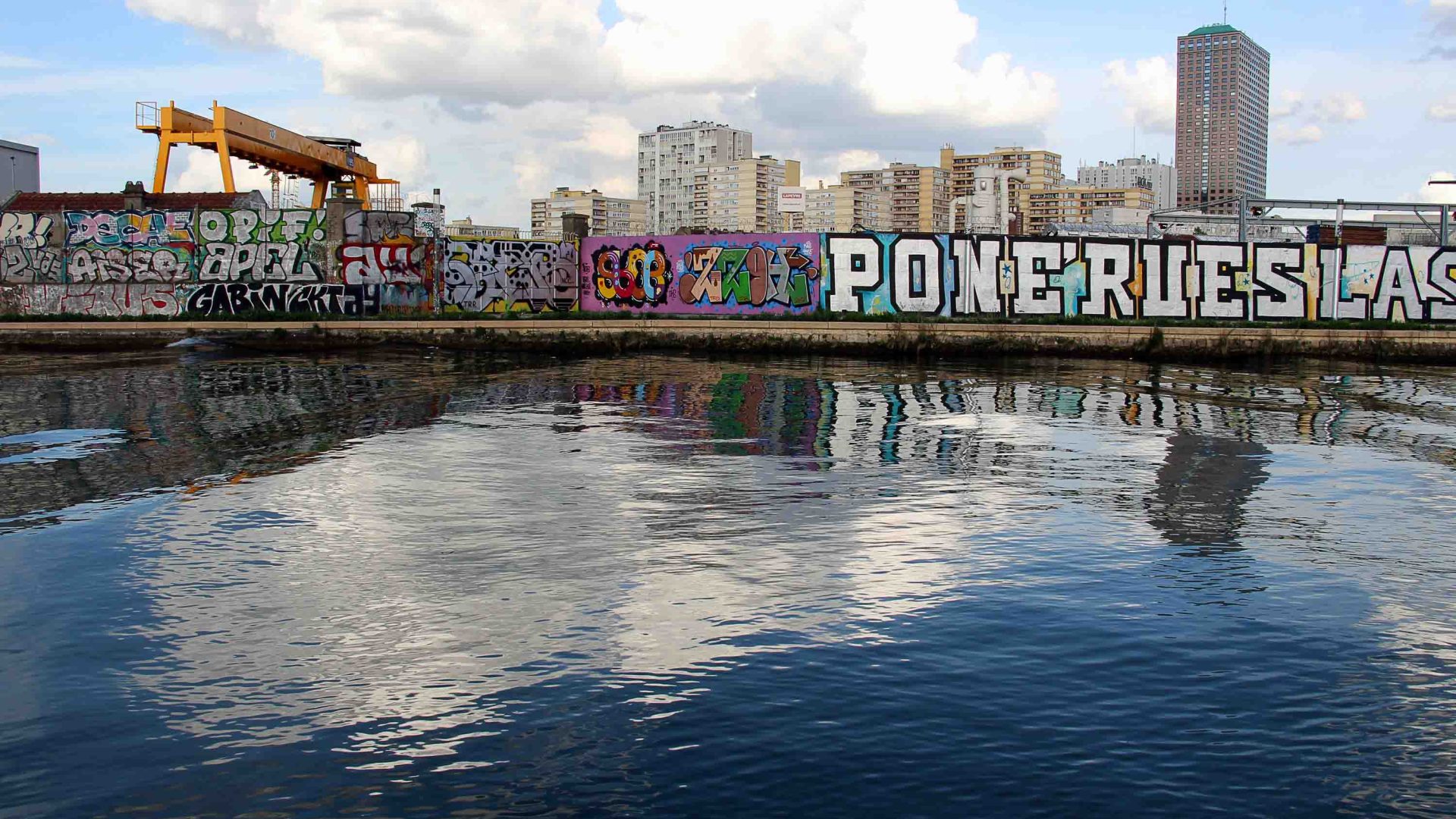 Grafiti above the water of the canal and buildings in the background.