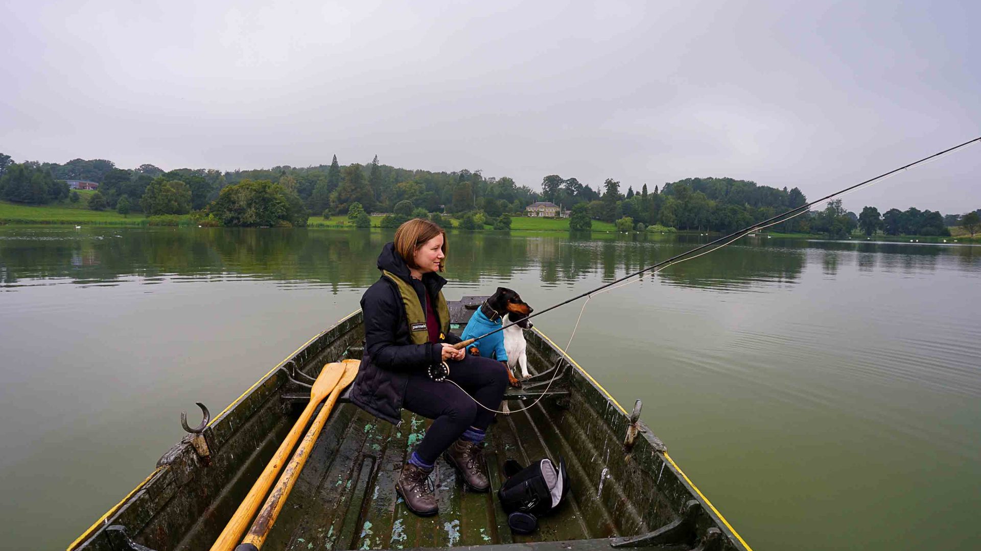 A woman and two dogs are fishing in a small boat.