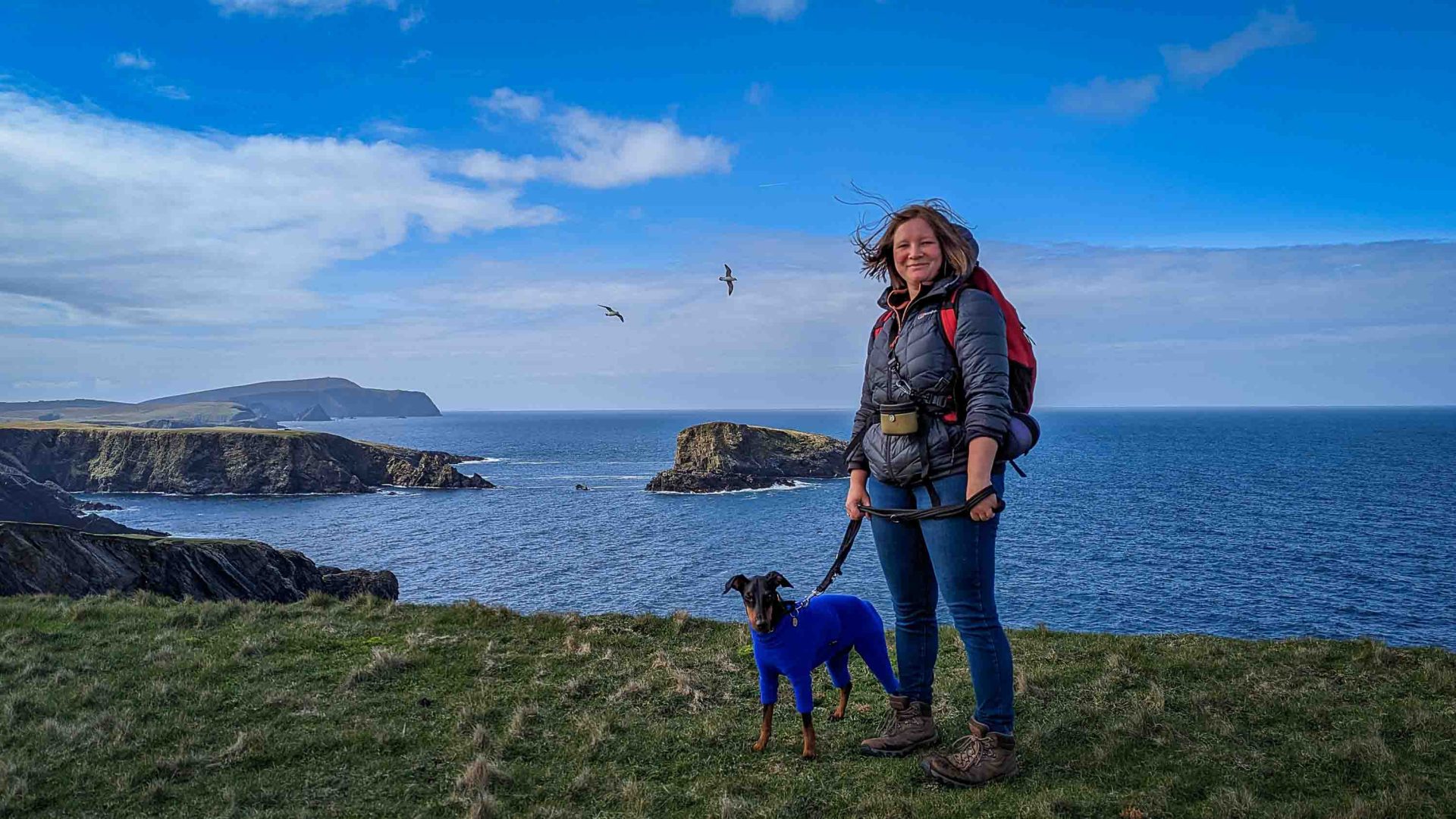 Lottie and her dog stand in front of a body of blue water.