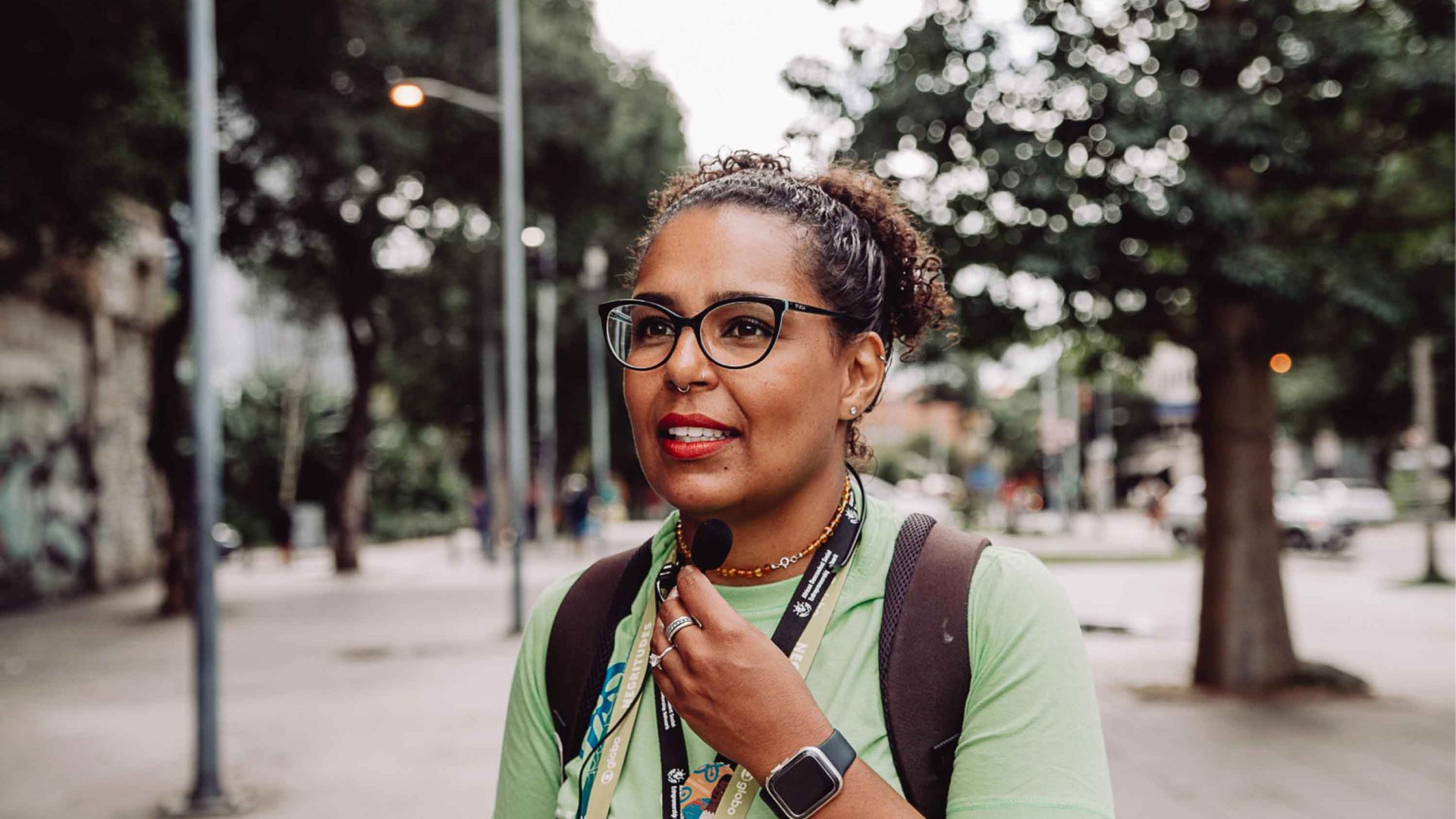 Guide Lua Ferreira on a tour. She stands in a square and holds a small microphone.