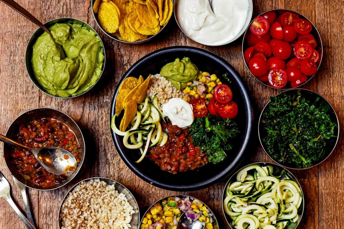 Looking down on a range of vegetarian foods and a bowl of all ingredients together in the centre.