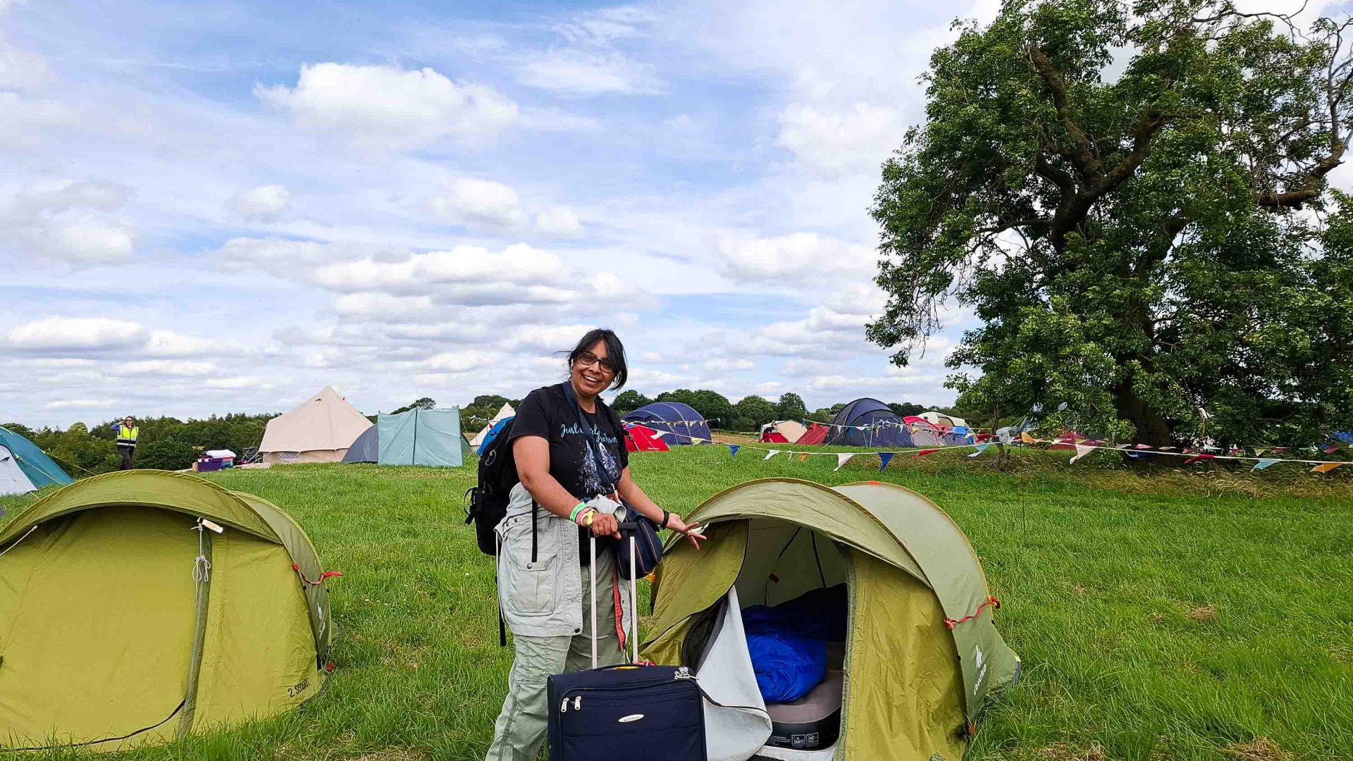 Dhruti stands in front of her green tent with a suitcase and a backpack.