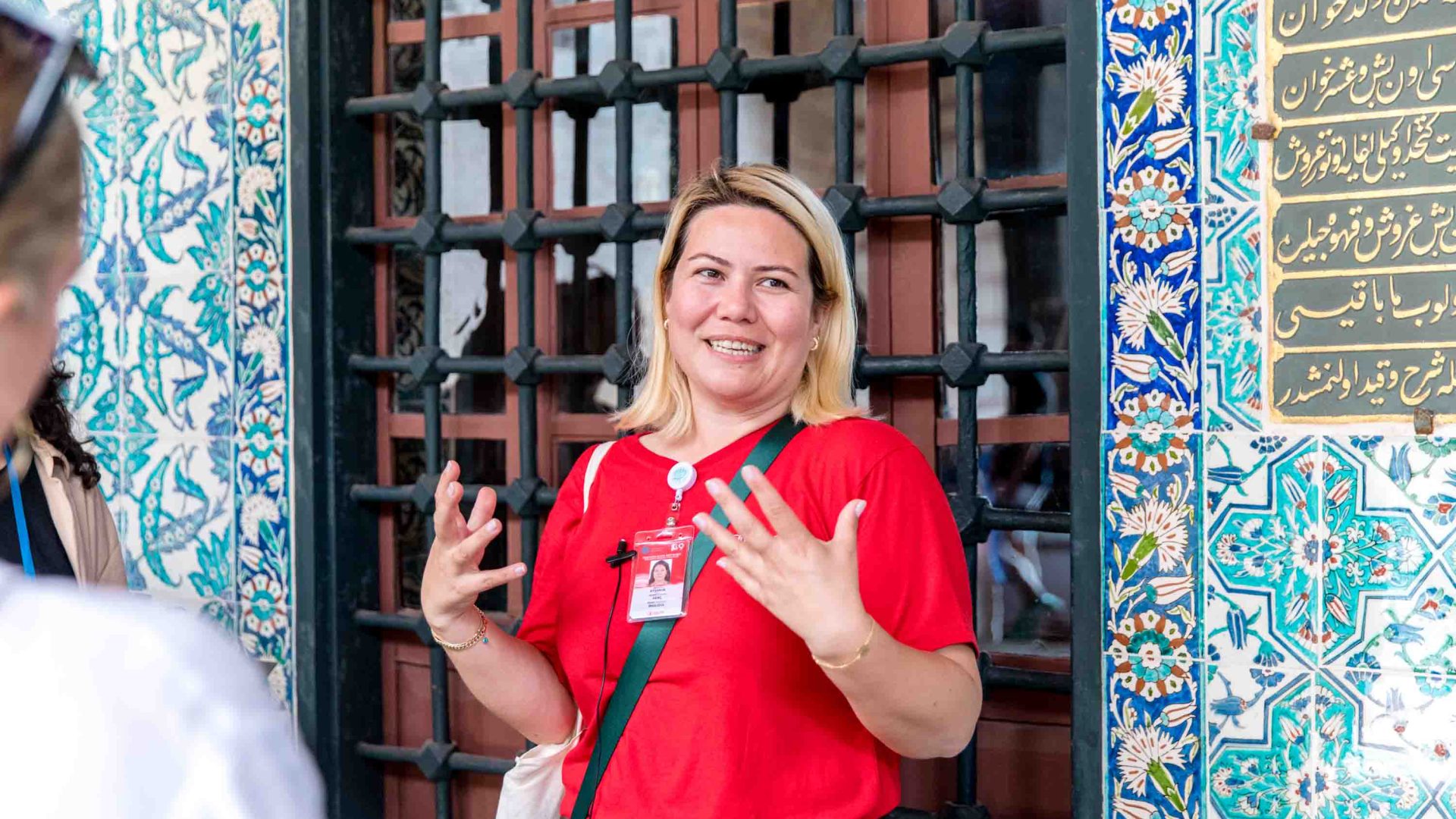 A tour guide with blonde hair and a red shirt talks animatedly.