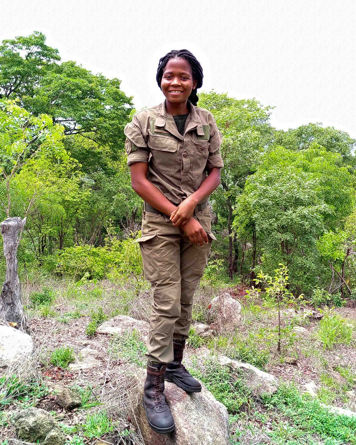 A ranger stands on a rock near trees.