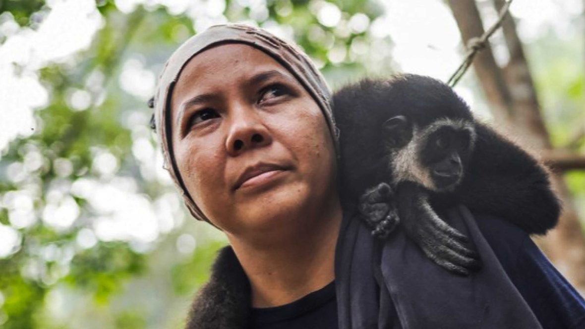 A woman looks away while she has a gibbon on her shoulder.